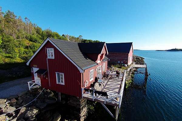 Rotes Holzhaus direkt am Wasser in Hitra, Norwegen. Perfekter Ausgangspunkt für Angelreisen und Abenteuer. Malerische Landschaft, klares Meer, entspannte Atmosphäre – ideal für Erholung und erfolgreiche Angeltrips.