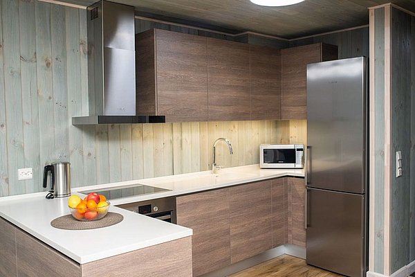Moderne Küche in Nord-Norwegen mit Holzwänden, hochwertigen Holzschränken, Edelstahlgeräten und heller Arbeitsfläche. Ein Obstkorb fügt Farbakzente hinzu. Ideal für Angelreisende, die Komfort und Funktionalität suchen.