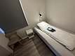 Einfaches, gemütliches Einzelzimmer in Hitra, Norwegen, mit Bett, Nachttisch, Lampe und Fenster mit Rolladen. Ideal für erholsame Nächte nach erlebnisreichen Angelabenteuern in der wunderschönen Umgebung.