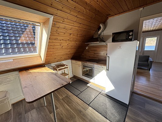 Gemütliche Ferienwohnung in Hitra, Norwegen: Dachgeschossküche mit Holzverkleidung, modernem Herd, Kühlschrank und Mikrowelle. Sonnendurchfluteter Essbereich mit Dachfenster, Blick ins Grüne. Ideal für Angelurlaub und Erholung in skandinavischer Natur.