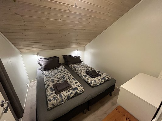 Gemütliches Schlafzimmer in Nord-Norwegen mit zwei Einzelbetten, Holzwänden und Decke. Ideal für erholsame Nächte nach einem spannenden Angelurlaub. Freundliche Atmosphäre lädt zum Entspannen ein. Perfektes Rückzugsziel in Norwegens atemberaubender Natur.