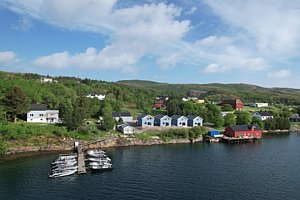 Idyllische Küstenlandschaft in Hitra, Norwegen: Boote am Steg, bunte Häuser vor grünen Hügeln. Perfektes Ziel für Angelurlaub, Naturfans und Erholungssuchende. Blauer Himmel und klare Gewässer versprechen Abenteuer und Entspannung in skandinavischer Schönheit.