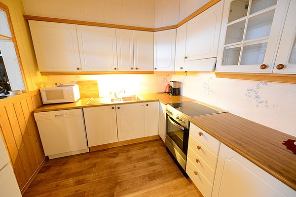 Gemütliche Küche in Nord-Norwegen mit weißen Schränken, Holzarbeitsflächen, Herd, Spüle und Mikrowelle. Heller Holzboden. Ideal für Selbstversorger beim Angelurlaub. Perfekt für komfortable Zubereitung frischer Fänge.