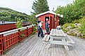 Eine Holzterrasse in der norwegischen Region Hitra, mit roten Gebäuden, grüner Umgebung und Picknicktisch. Ideal für Angelurlaub und Erholung. Ruhige, naturnahe Atmosphäre zum Verweilen in skandinavischer Landschaft.