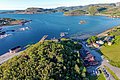 Luftaufnahme der malerischen Küstenlandschaft von Hitra, Norwegen: Klare blaue Gewässer, grüne Hügel, kleine Inseln und charmante Häuser bilden die perfekte Kulisse für Angelreisen und Naturerlebnisse. Ideal für ein unvergessliches Angelabenteuer.