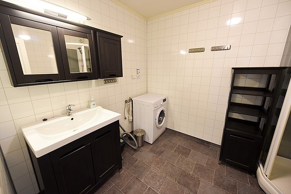Modernes Badezimmer in Hitra, Norwegen: Waschmaschine, schwarzer Waschtisch mit Spiegel, geflieste Wände, grauer Boden. Perfekt für komfortable Angelurlaube. Entspanne nach erfolgreichen Angeltagen in dieser gut ausgestatteten Unterkunft.