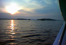 Sonnenuntergangsszene über einem ruhigen See mit Inseln im Hintergrund, vom Wasser aus betrachtet.