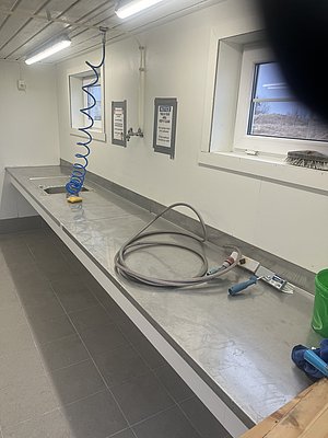 Moderner Reinigungsraum in Nordland, Norwegen: Edelstahl-Arbeitsfläche mit Spüle, Schlauch, Fenster, Beleuchtung und Hinweisschildern. Ideal für Angelreisen, um den Fang sicher und hygienisch zu säubern. Perfekt für Meeresangeln-Abenteuer.