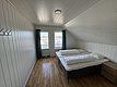 Gemütliches Schlafzimmer in Hitra, Norwegen: Helles Holzinterieur, Doppelbett mit weißen Bettdecken, Fenster bietet malerischen Blick auf Dächer. Perfekt für Angelurlauber, die Komfort und Erholung suchen. Ideal gelegen für Meeresangeln-Abenteuer.