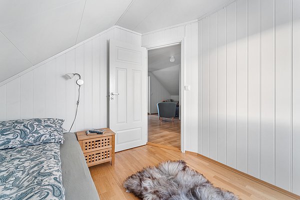 Gemütliches Skandinavisches Schlafzimmer in Nordnorwegen mit weißen Holzwänden, Holzfußboden, Bett mit blauem Muster, Nachttisch und offener Tür zum Wohnbereich. Ideal für Angelurlaub und Entspannung in natürlicher Umgebung.