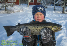Ein Kind hält eine gefangene Forelle im verschneiten Winterwunderland.