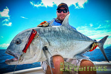 Ein Angler hält stolz einen großen Giant Trevally auf einem Boot vor der Küste Tansanias. Strahlend blauer Himmel und Meer im Hintergrund. Abenteuerliches Meeresangeln in Ostafrika.
