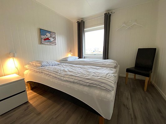 Helles, gemütliches Schlafzimmer in Nord-Norwegen mit Doppelbett, maritimer Dekoration, und Fensterblick. Ideal für erholsamen Angelurlaub, kombiniert Komfort mit skandinavischer Schlichtheit. Perfekte Unterkunft für Abenteurer und Ruhesuchende.