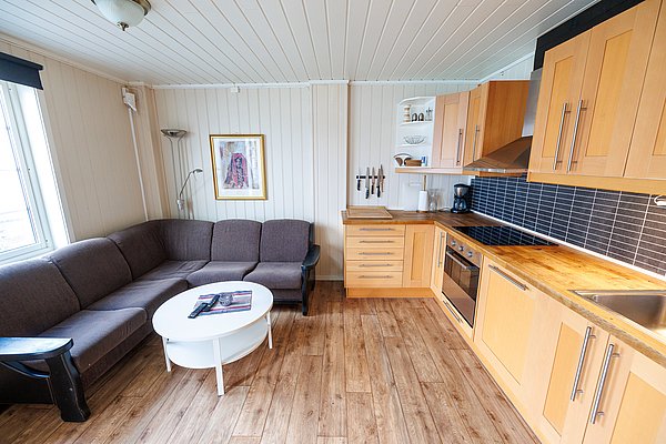 Gemütliche Ferienwohnung in Nordland, Norwegen: Moderne Küche mit Holzschränken, bequeme Sofaecke, stilvolle Einrichtung. Perfekt für Angelreisende, die Komfort und Entspannung inmitten der atemberaubenden norwegischen Landschaft suchen. Ideal für Erholung nach einem erfolgreichen Angeltag.