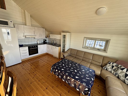 Gemütliches Apartment auf Hitra, Norwegen mit moderner Küche, komfortabler Ledercouch und maritim dekoriertem Tisch. Ideal für Angelreisen mit Wohlfühlfaktor. Helle Holzwände und Fenster sorgen für eine einladende Atmosphäre.