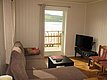 Gemütliches Wohnzimmer in Nord-Norwegen mit Sofa, Fernseher und Balkonblick auf fjordähnliche Landschaft. Ideal für Angelurlaub und Entspannung in ruhiger Umgebung. Perfekter Ausgangspunkt für Abenteuer und Erholung beim Angeln.