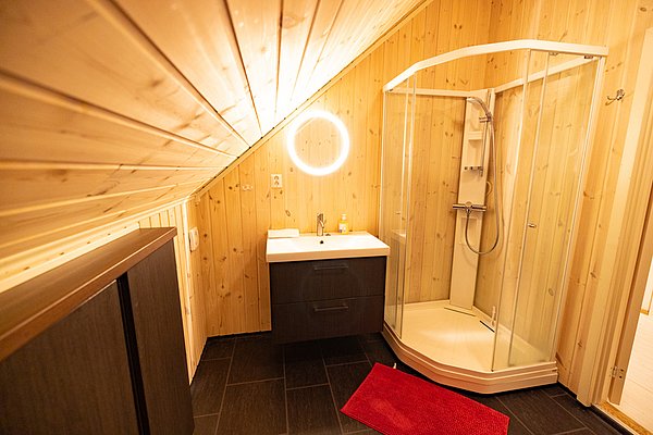 Gemütliches Badezimmer in Nordland, Norwegen: Holzverkleidung, moderne Dusche, Waschbecken mit beleuchtetem Spiegel. Ideal für erholsame Angelurlaube. Skandinavisches Design trifft auf Funktionalität für nachhaltigen Komfort.
