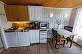 Gemütliche Ferienhausküche auf Hitra, Norwegen. Moderne Ausstattung mit Herd, Mikrowelle und Kaffeemaschine. Essbereich für zwei Personen, rustikaler Charme durch Holzelemente. Ideal für erholsame Angelurlaube in der malerischen Umgebung.