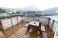 Nordland, Norwegen: Eine regennasse Terrasse mit Holztisch und Bänken, umgeben von malerischen Bergen und Küstenblick. Perfekt für Angelreisen mit eindrucksvoller Naturlandschaft und entspannten Momenten in rustikaler Umgebung.