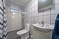 Modernes, gefliestes Badezimmer in Nord-Norwegen mit Dusche, Waschbecken und WC. Helle Kacheln und ein kleines Fenster schaffen eine freundliche, saubere Atmosphäre. Ideal für erholsame Unterkünfte beim Angelurlaub.