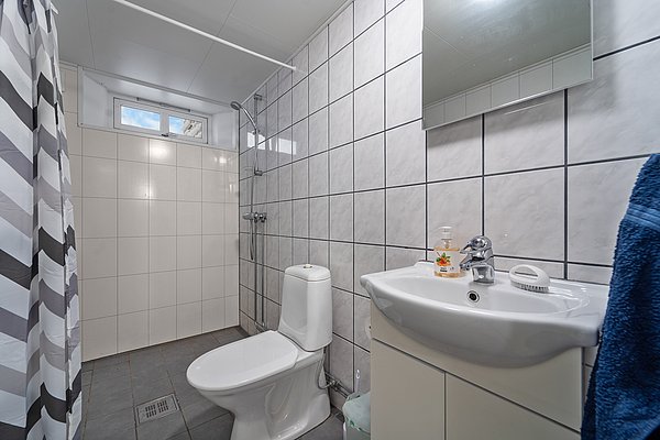 Modernes, gefliestes Badezimmer in Nord-Norwegen mit Dusche, Waschbecken und WC. Helle Kacheln und ein kleines Fenster schaffen eine freundliche, saubere Atmosphäre. Ideal für erholsame Unterkünfte beim Angelurlaub.