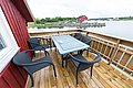 Gemütliche Terrasse in Nordland, Norwegen, mit Blick auf ein ruhiges Gewässer und rotes Haus im Hintergrund. Perfekt für Angelurlaub und Entspannung. Holzterrasse mit Tisch und vier Stühlen.