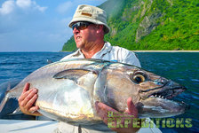 Ein Angler hält stolz einen großen Thunfisch an der Küste Tansanias. Im Hintergrund tropische Landschaft und blaues Meer. Perfektes Reiseziel für begeisterte Angler. Optimiert für Angelurlaub und Meeresangeln in Afrika.