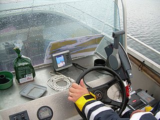 Eine Person steuert ein Motorboot bei Regen mithilfe eines Kartenplotters und anderer Navigationsinstrumente.