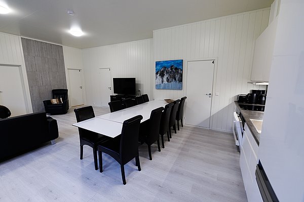 Moderner Aufenthaltsraum in Nordland, Norwegen, mit langen Esstischen, schwarzen Stühlen und heller Küche. Perfekte Unterkunft für Angelreisen und Entspannung. Ideal für Abenteuer und Komfort in skandinavischer Natur.