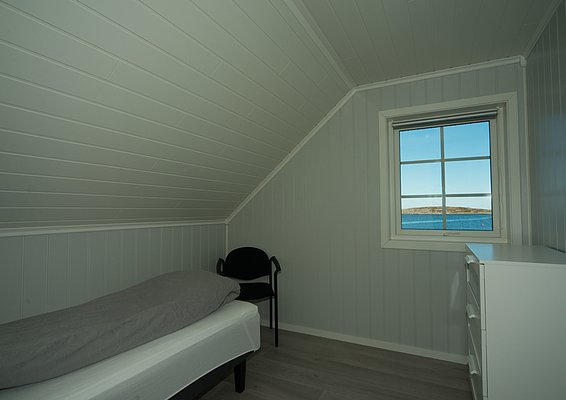 Gemütliches Schlafzimmer auf Hitra, Norwegen, mit Einzelbett, maritimem Ambiente. Fensterblick auf das Meer sorgt für Entspannung und Abenteuerlust. Ideal für Anglerurlauber. Helle, freundliche Holzwände und -decken bieten skandinavischen Charme.