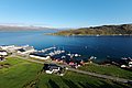 Luftaufnahme eines idyllischen Hafens in Nord-Norwegen: klare blaue Gewässer, ankernde Boote, grüne Landschaft und farbenfrohe Häuser entlang der Küste. Perfekt für Angelreisende und Naturliebhaber.