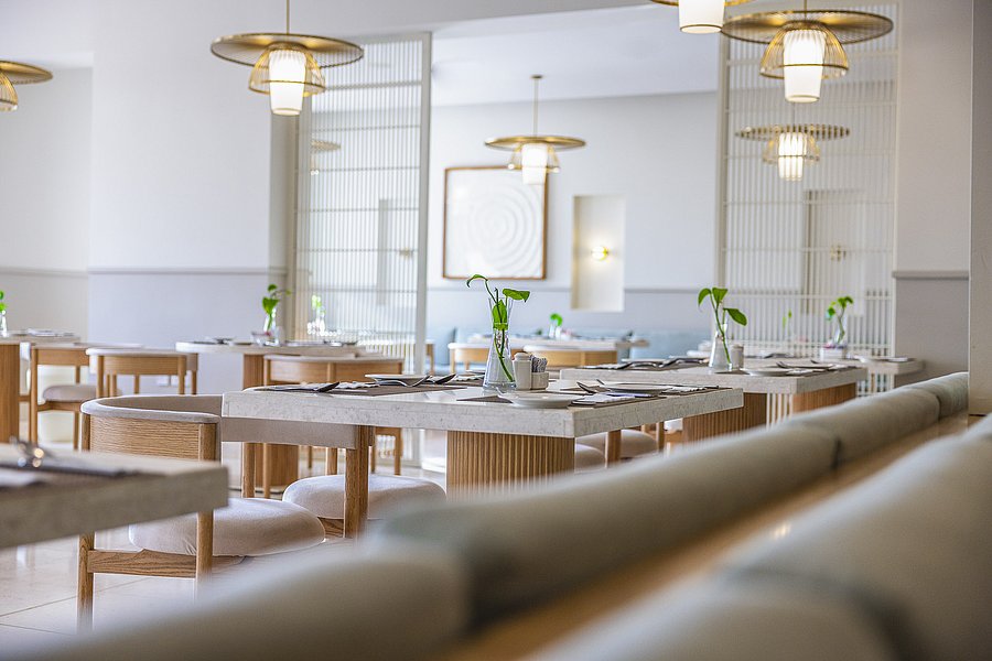 Modernes Restaurant in Süd-Norwegen mit minimalistischer Einrichtung: helle Holzmöbel, stilvolle Beleuchtung, dezente Tischdekoration mit grünen Akzenten. Einladendes Ambiente für Genussmomente bei einer Angelreise in Norwegen.
