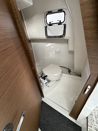 Kompakte Kajüten-Toilette auf einem Boot in Süd-Norwegen, mit Bullauge und Holzverkleidung, ideal für Angelreisen. Komfortable Ausstattung sorgt für Bequemlichkeit während deiner Abenteuer auf dem Meer.