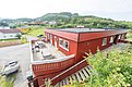 Rotes, traditionelles Holzgebäude in Hitra, Norwegen, mit Terrasse und Picknicktischen. Umgeben von grüner Landschaft und Häusern. Ideal für erholsamen Angelurlaub in idyllischer Umgebung. Perfekt für Naturliebhaber und Abenteuerlustige.