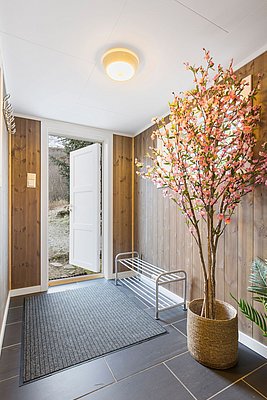 Heller Eingangsbereich in Nordland, Norwegen: Offene Tür mit Blick ins Freie, Holzverkleidung, Schuhregal und dekorativer Baum mit rosa Blüten in einem Korb, einladend und modern gestaltet.