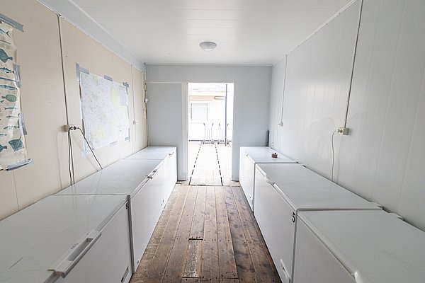 Kühlraum in Nord-Norwegen mit mehreren Gefriertruhen, perfekt zur Lagerung großer Fischfänge nach erfolgreichem Angelabenteuer. Holzfußboden und Karten an der Wand verleihen dem Raum rustikalen Charme. Ideal für Angler auf Angelreise.