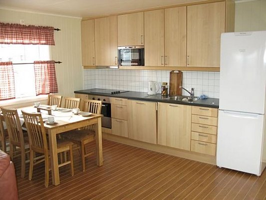 Gemütliche skandinavische Küche in Nordland, Norwegen: Holzfronten, Esstisch mit vier Stühlen, heller Kühlschrank, und moderne Ausstattung. Perfekt für Angelurlauber, die Komfort und Funktionalität schätzen. Ideal für gemeinsame Mahlzeiten nach erfolgreichen Angelausflügen.