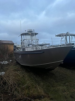 Aluminium-Boot auf bewachsener Fläche in Südwest-Norwegen, bereit für Angelabenteuer. Wolkenverhangener Himmel sorgt für nordischen Charme. Ideal für Angelreisen und Meeresangeln im malerischen norwegischen Fjordland.