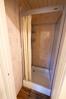 Kompakte Duschkabine in einer gemütlichen Unterkunft in Nordland, Norwegen. Holzfußboden und helle Wände sorgen für ein heimeliges Ambiente, ideal nach einem langen Angeltag. Perfekte Kombination aus Funktionalität und Komfort.