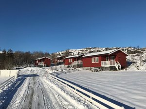 Rote Holzhütten in verschneiter Landschaft in Nordland, Norwegen, unter klarem blauem Himmel. Ideal für winterliche Angelreisen und Naturerlebnisse. Perfekte Unterkunft für entspannende Urlaube in idyllischer Umgebung.