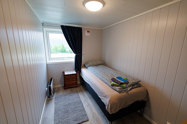 Gemütliches Einzelzimmer in Nord-Norwegen mit modernem Design. Helles Fenster blickt auf grüne Landschaft. Ideal für Angelurlaub, mit komfortablem Bett und einladender Atmosphäre. Perfekt zum Entspannen nach einem spannenden Angeltag.