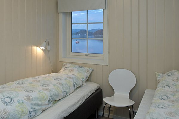Gemütliches Schlafzimmer mit zwei Einzelbetten, einem Stuhl und einem Fenster mit Blick auf ruhige Gewässer und Berge im Hintergrund.