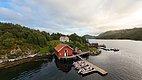 Küstenlandschaft in Hitra, Norwegen: Rote Fischerhütten mit Bootssteg am ruhigen Fjord, umgeben von grünen Wäldern und Bergen. Perfekter Angelurlaubsort für Naturliebhaber und Abenteurer. Ideal für Angelreisen und maritime Erkundungen.