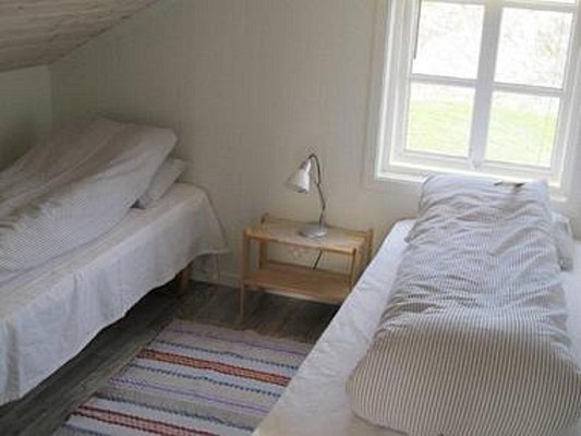 Gemütliches Schlafzimmer in Nordland, Norwegen: Zwei Einzelbetten mit gestreifter Bettwäsche, heller Holzboden, bunte Teppiche und ein Fenster mit Blick auf Natur. Perfekt für erholsame Nächte nach einem erlebnisreichen Angeltag.