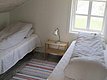 Gemütliches Schlafzimmer in Nordland, Norwegen: Zwei Einzelbetten mit gestreifter Bettwäsche, heller Holzboden, bunte Teppiche und ein Fenster mit Blick auf Natur. Perfekt für erholsame Nächte nach einem erlebnisreichen Angeltag.