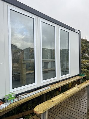 Modernes Gebäude in Nordland, Norwegen, mit großen Fenstern und Holzgeländer. Ideal für Angelreisen, bietet es eine gemütliche Aussicht auf die umliegende Landschaft. Perfekte Kombination aus Natur und Komfort.