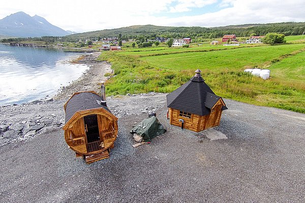Hölzerne Sauna und Grillhütte in malerischer Küstenregion Nord-Norwegens, umgeben von Bergen und grünen Feldern. Perfekter Ort für Entspannung und Abenteuer.