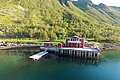 Rotes Fischerhaus am Fjord in Nord-Norwegen, umgeben von grünen Hügeln. Perfektes Reiseziel für Angelurlaub, entspannte Naturerlebnisse und unvergessliche Meeresabenteuer. Ideal für alle, die Erholung und Abenteuer suchen.