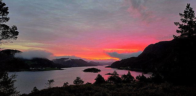 Sonnenuntergang über der Küstenlandschaft von Hitra, Norwegen. Der Himmel leuchtet in intensiven Rosatönen über den stillen Gewässern und bewaldeten Hügeln, ideal für unvergessliche Angelreisen und Naturerlebnisse. Friedliche Atmosphäre und atemberaubende Aussichten.