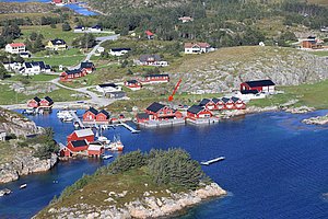 Küstenlandschaft in Hitra, Norwegen: Rote Fischerhütten säumen eine blaue Bucht, umgeben von grünen Hügeln. Idyllischer Ort für Angelreisen mit malerischen Ausblicken und reicher Tierwelt. Perfekt für Meeresangeln und Erholung.